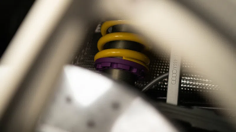 Mechanic with gray cap working on yellow car suspension and brake system inside red vehicle wheel well.