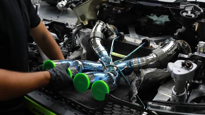 Mechanic installing shiny chrome turbocharger piping with green caps in a high-performance car engine bay.