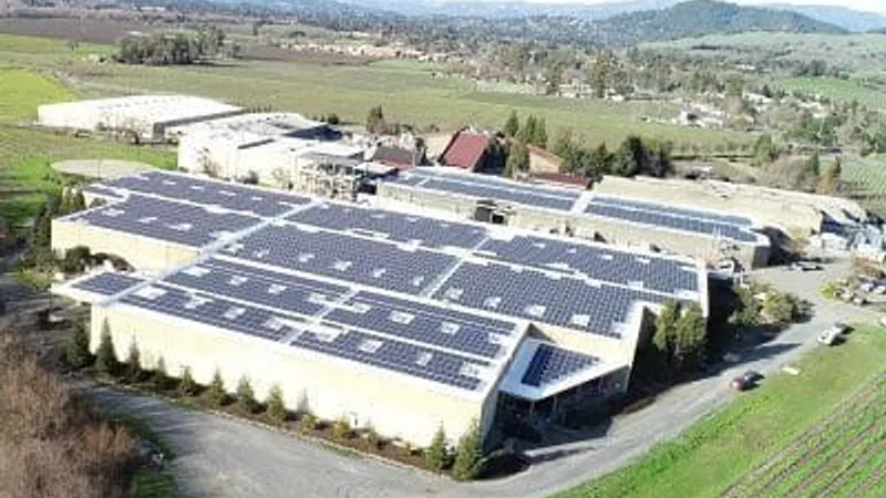 Large industrial buildings with solar panels on rooftops surrounded by fields and hills in the distance