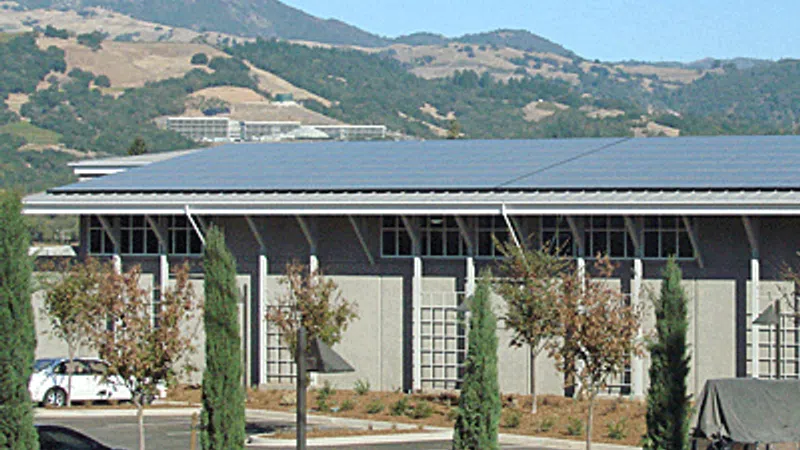 Commercial building with solar panels on roof surrounded by trees and parked cars under clear blue sky.