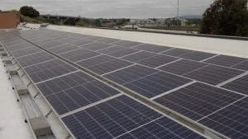 Solar panels installed on a flat rooftop under cloudy sky with distant urban and natural landscape.