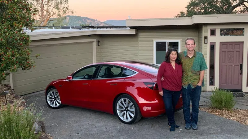 a man and woman standing next to a red car in front of a house