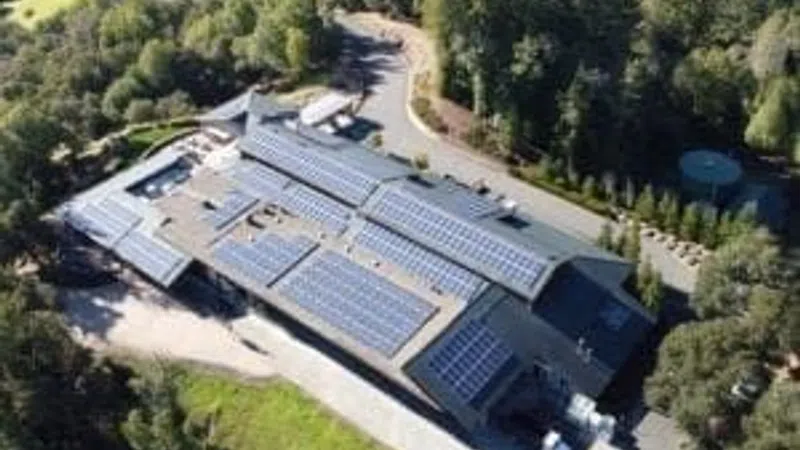Aerial view of a large building with solar panels on the roof surrounded by trees and greenery.