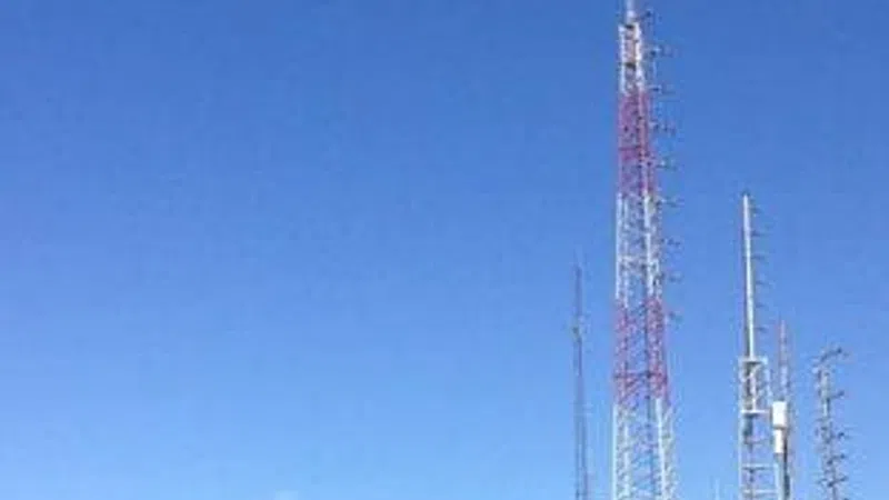 Communication towers with antennas on a hill under a clear blue sky with solar panels nearby