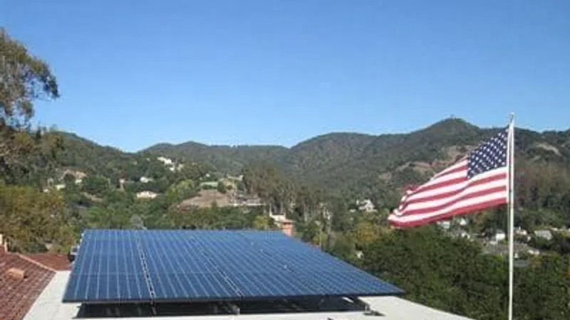 Solar panels installed on a rooftop with an American flag beside them and hills in the background under a clear sky.