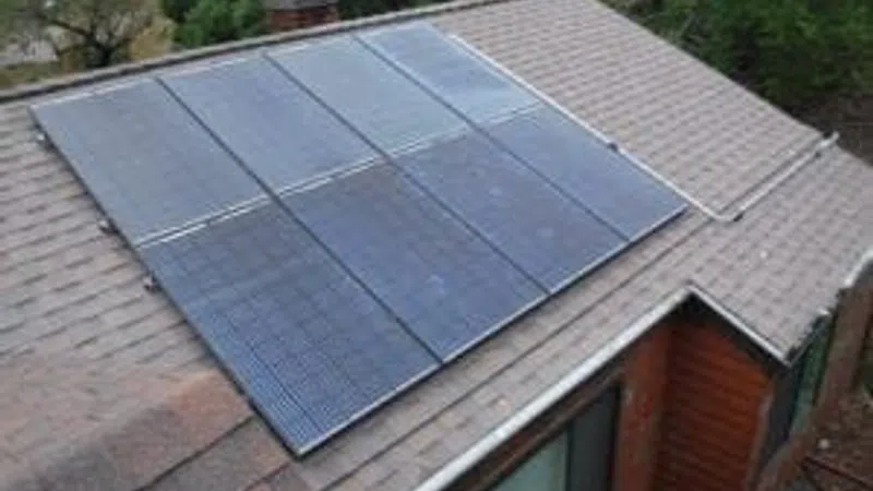 Solar panels installed on a residential shingled roof surrounded by trees and greenery.