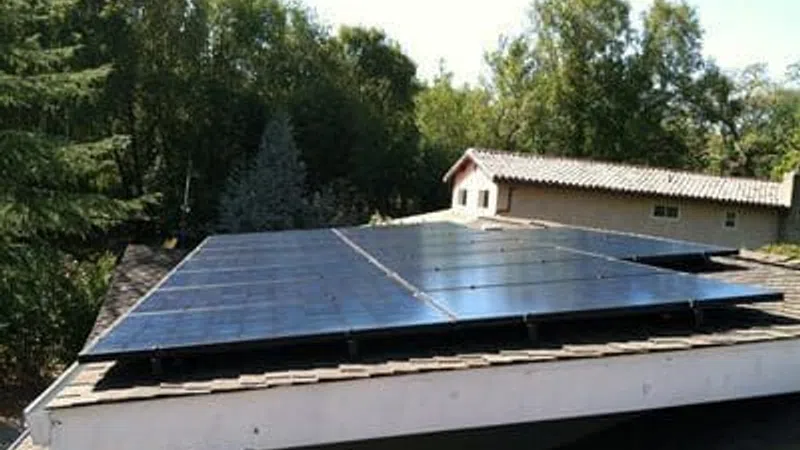 Solar panels installed on residential rooftop surrounded by trees under clear sky