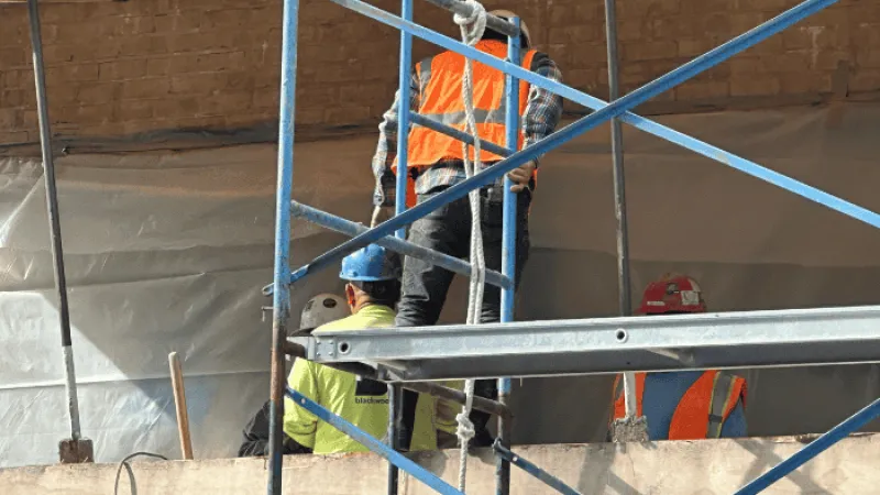 Construction workers wearing safety gear working on scaffolding at a building site under renovation.