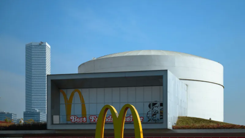Modern McDonald's restaurant building with large golden arches and city skyscraper in background under clear sky