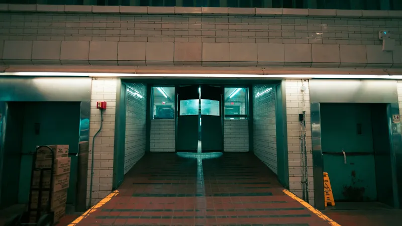 Dimly lit industrial hallway with tiled walls, double swinging doors, and delivery equipment at night.