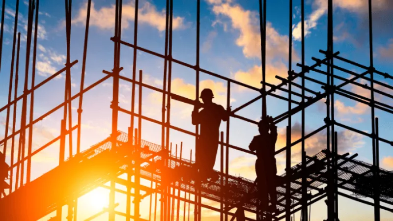 Silhouettes of construction workers on scaffolding at sunset with vibrant sky and clouds.