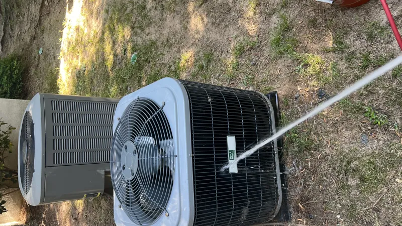 Technician testing outdoor air conditioning unit's efficiency with a digital gauge on a sunny lawn with tools nearby.