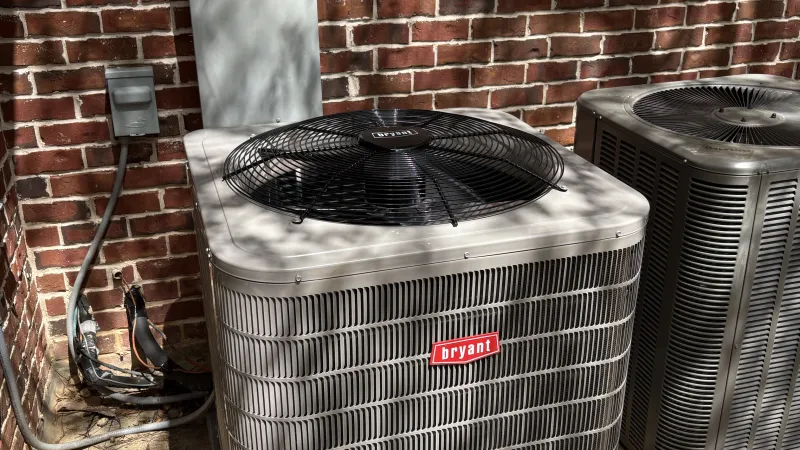 Two outdoor air conditioning units by a brick wall, one branded Bryant and an electrical panel labeled Generac.