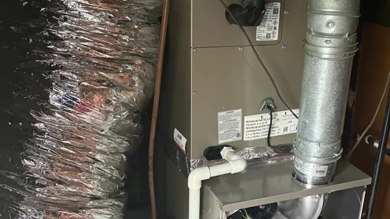 Open HVAC furnace unit with visible wiring, ductwork, and pipes in a basement setting with insulation.