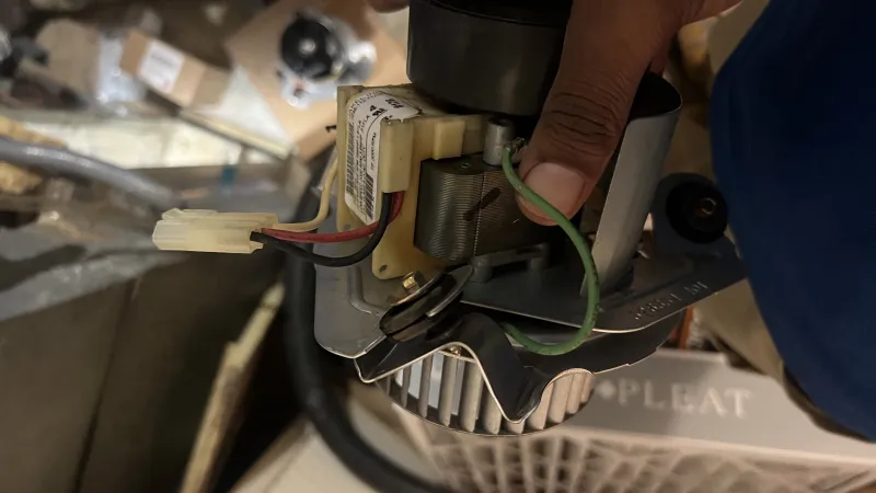 Hand holding electrical HVAC component with wires and metal parts in an indoor utility space.