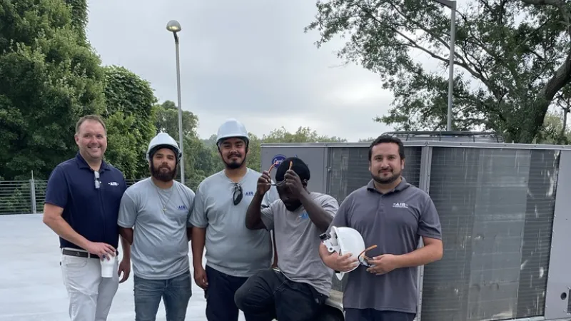 Group of five HVAC technicians posing with equipment on a rooftop under cloudy sky