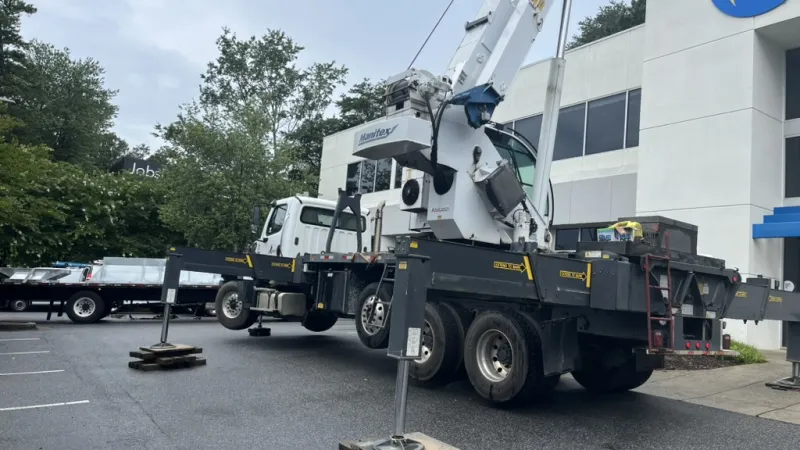 Mobile crane with extended stabilizers parked outside an office building on asphalt parking lot.