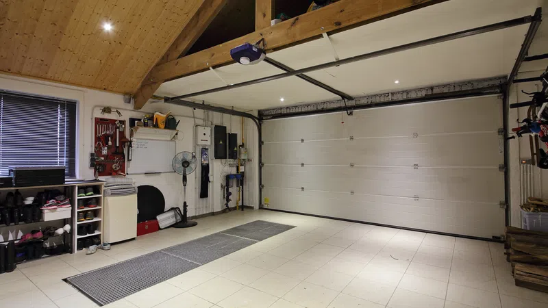 Spacious, clean garage interior with light tiled floor, overhead wooden beams, and organized storage on walls.
