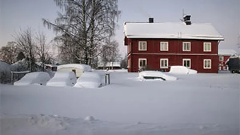 a red house with snow on the ground and trees in the back