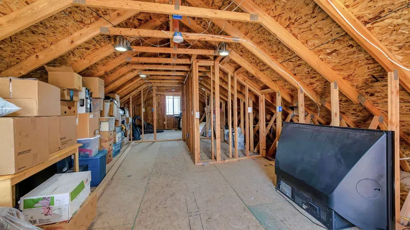 Spacious attic with exposed wooden beams, boxes, storage bins, and a flat-screen TV leaning against the wall.