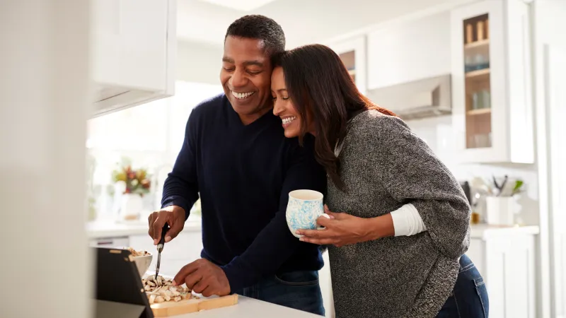 A happy couple prepares dessert together in a bright, modern kitchen, sharing smiles and a cozy moment.