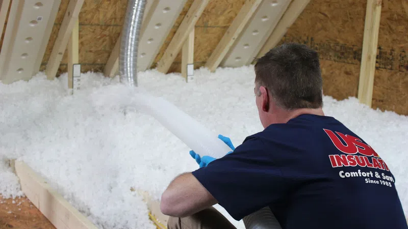 Worker installing loose-fill insulation in attic using a hose to improve home energy efficiency.
