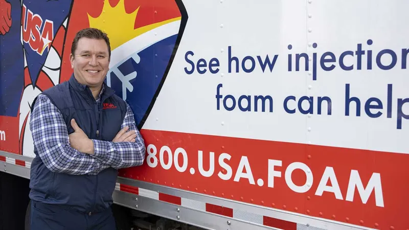 Smiling man in a blue vest stands next to a truck displaying USA Foam advertising campaign.