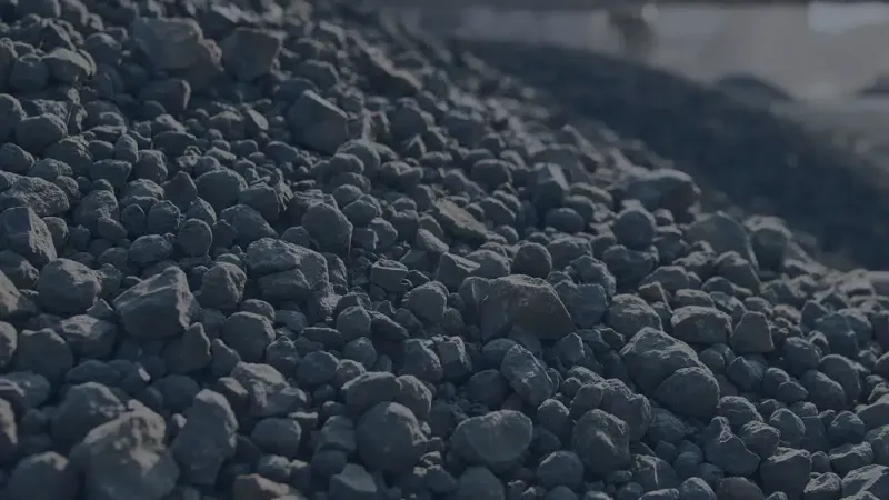 Large pile of coal stones with industrial structure blurred in the background under daylight.