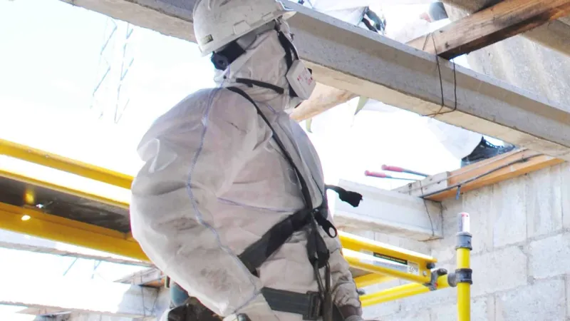 Worker in protective suit and helmet using bolt cutters on a yellow scaffold at construction site.