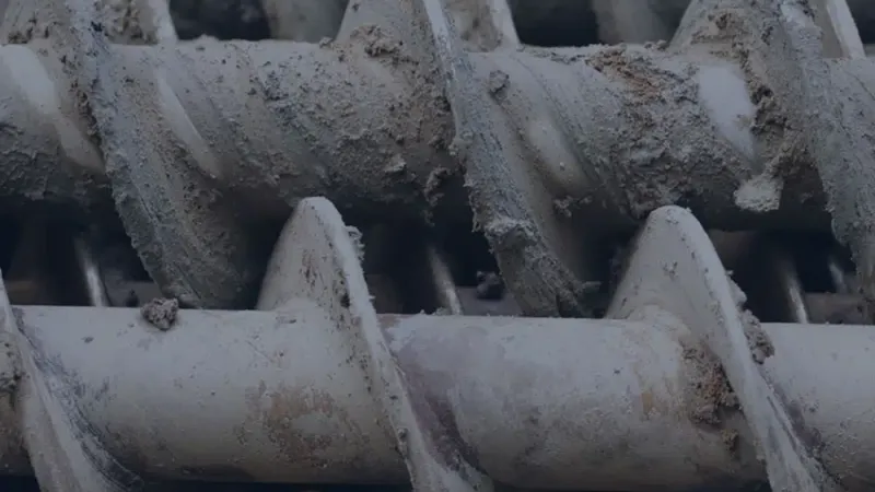 Close-up of dirty, worn metal auger screws covered in soil or dust in an industrial setting
