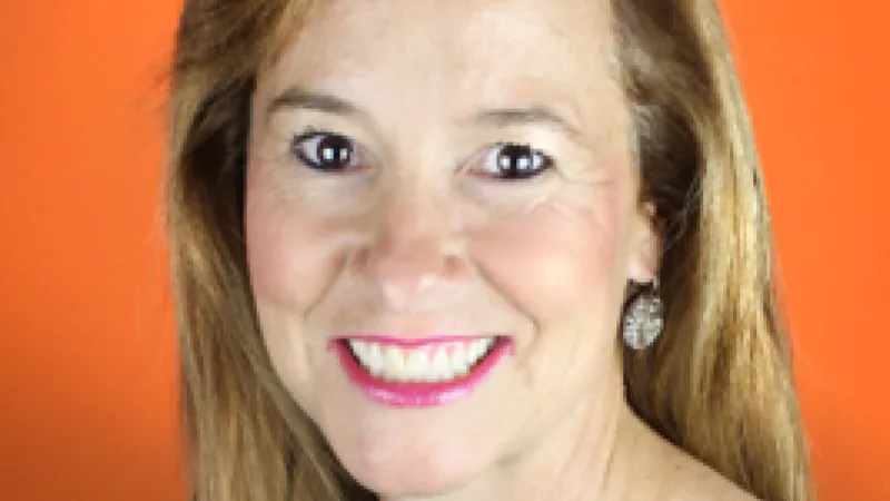 Smiling woman with long light brown hair wearing black top and earrings against an orange background
