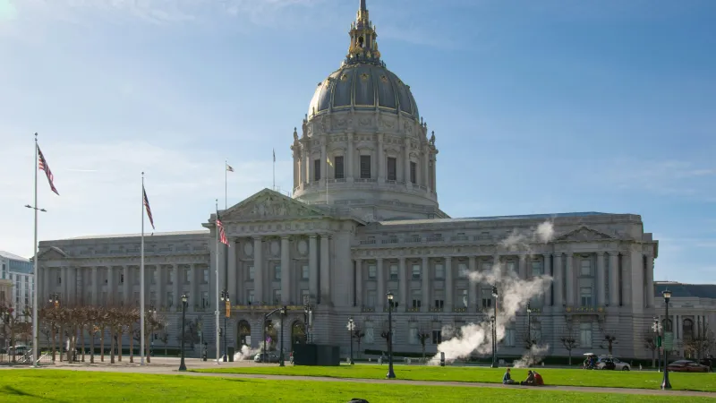 Historic government building with large dome and columns under clear blue sky, green lawn in foreground