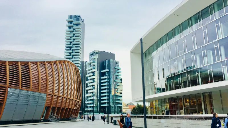 Modern urban plaza with contemporary buildings, wooden facade, glass architecture, and people walking on a cloudy day