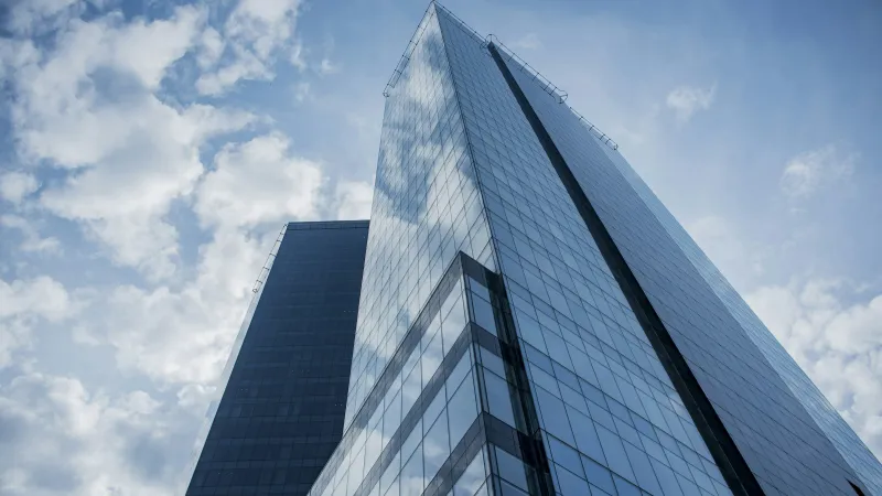 Glass skyscraper reflecting cloudy blue sky shot from ground looking up, modern architecture and urban cityscape.