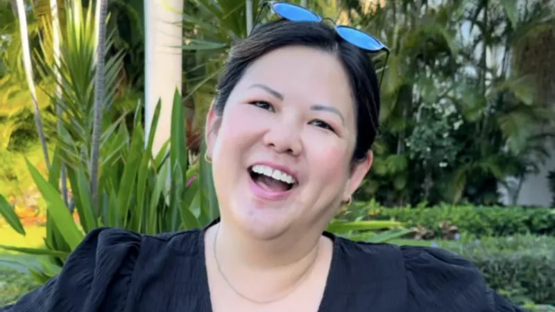 Smiling woman outdoors wearing a black top with puffed sleeves and sunglasses on head in lush garden setting.