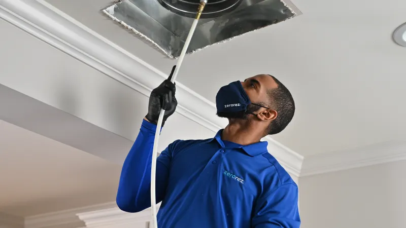 a man wearing a blue shirt and gloves and Zerorez® face mask cleaning a ventilation system to remove air duct smell and vent odors