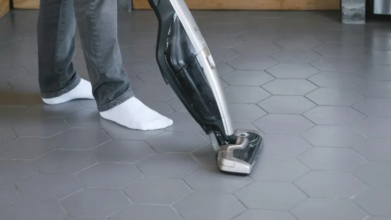 socked feet standing on a gray hexagon tile floor using a vacuum on tile