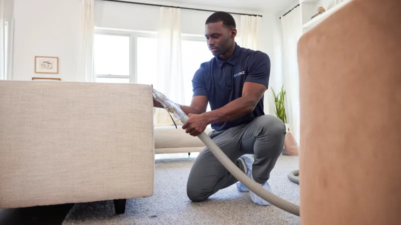 a Zerorez® technician professionally cleaning a couch in a living room