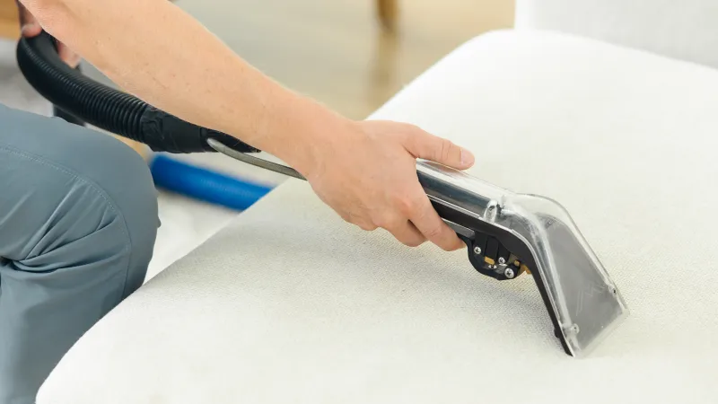 a Zerorez technician holding an upholstery tool on a white couch to help clean it as part of the carpet beetle removal process in a home for furniture and upholstery