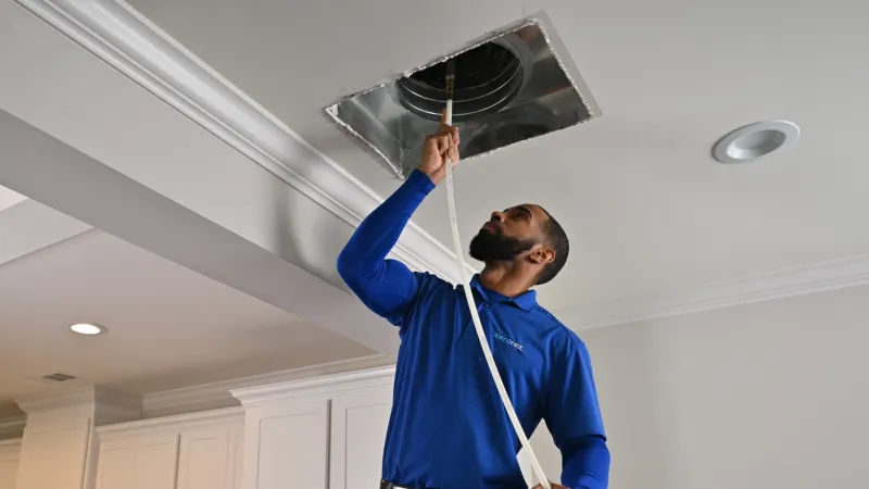 a male Zerorez air duct cleaning technician holding up an air duct cleaning hose into a ceiling air duct return register vent holding a fan