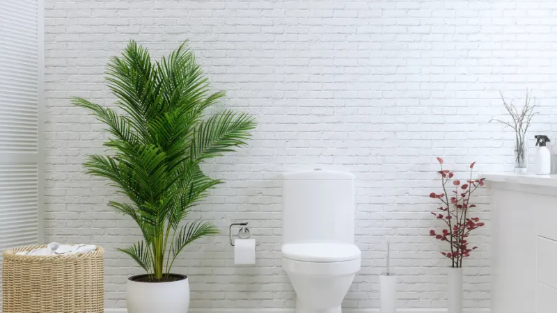 a toilet and potted plants on a white tile floor with white grout