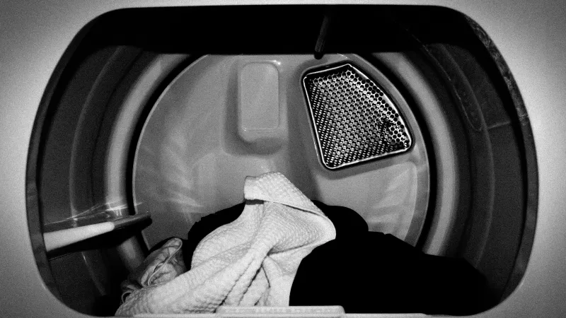 Black and white image inside an open dryer with a small amount of fabrics inside of it, dried