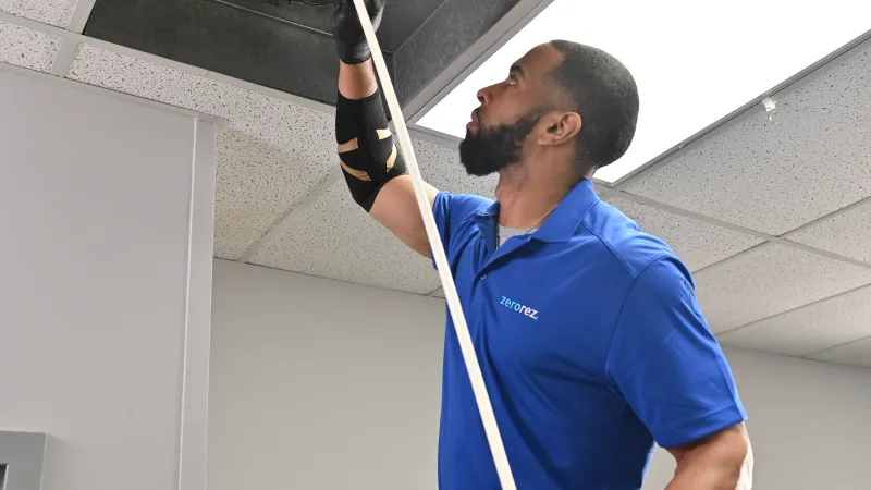 a male Zerorez air duct cleaning technician holding up an air duct cleaning hose into a ceiling air duct return register vent
