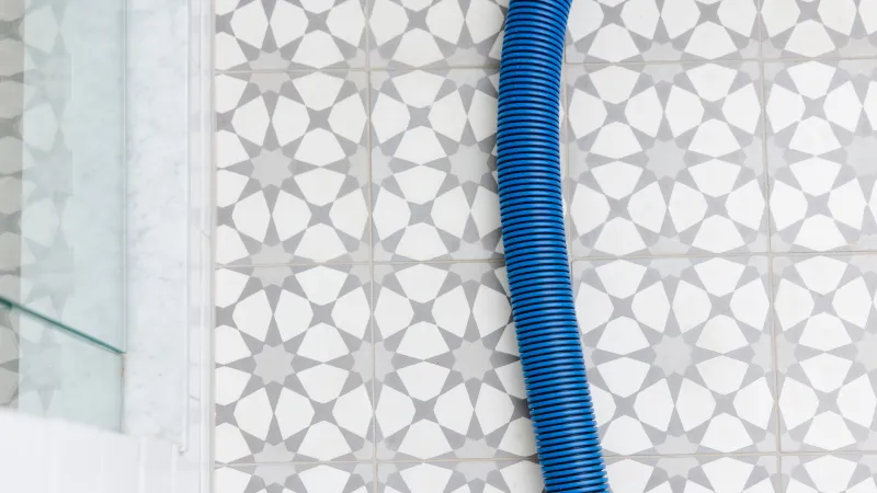 a blue Zerorez cleaning hose on a white and gray patterned tile bathroom floor