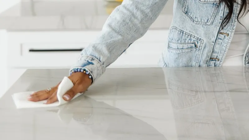 a woman cleaning and wiping down her white countertop in her white kitchen as part of her spring cleaning checklist