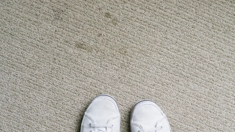 a pair of white shoes on standing on a dirty stained olefin carpet