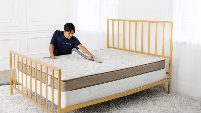 a male Zerorez technician using an upholstery tool to professionally clean a mattress in a bedroom