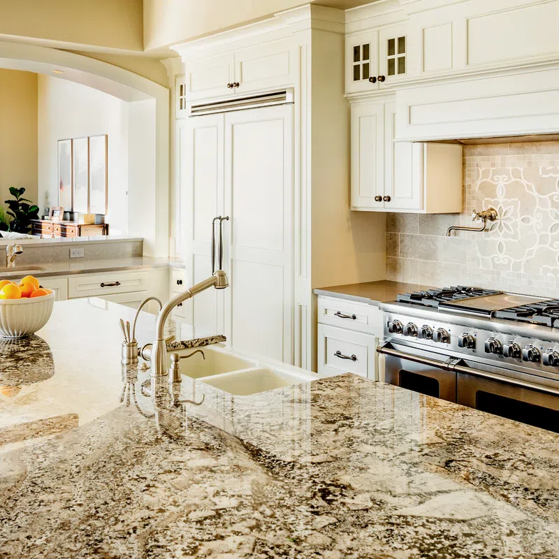 Bright kitchen with white cabinets, granite countertops, stainless steel stove, and decorative tile backsplash.
