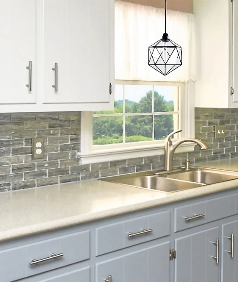 Modern kitchen with white and gray cabinets, gray glass tile backsplash, beige countertop, and double sink under window.