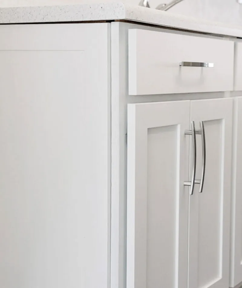 White modern kitchen cabinets with stainless steel handles under a light countertop and wood flooring.